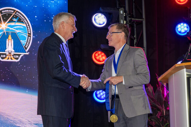 Two men in business attire shake hands during a ceremony